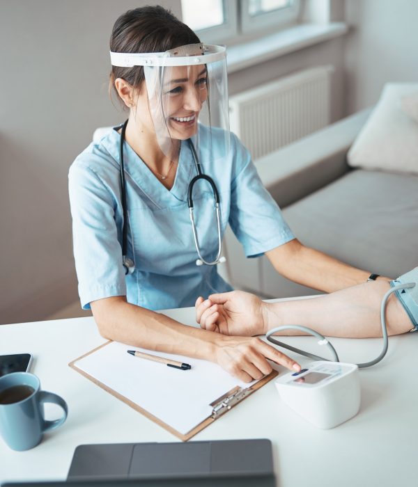 Joyful doctor in face mask checking patient blood pressure